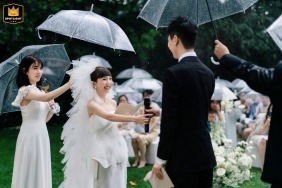 At the wedding venue called Ai Jiangshan in Beijing, China, the bride leans in and hands the microphone to the groom while standing together in the rain.